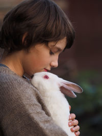 Cute little boy in gray knitted sweater holds a small white rabbit in his arms