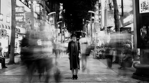 Full length of young woman standing on busy street in city at night