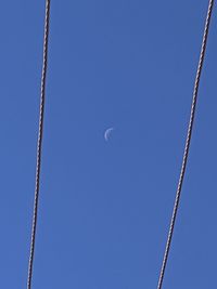 Lunar ghost moon between power lines against a clear blue sky