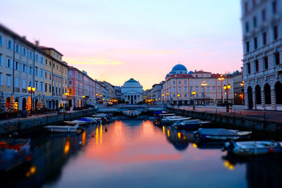 Boats moored at canal amidst buildings against sky at dusk