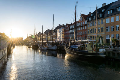 Sailboats moored on canal amidst buildings in city against sky