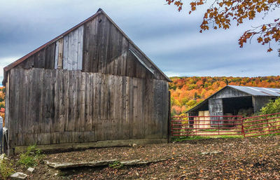 Barn by houses on field against sky