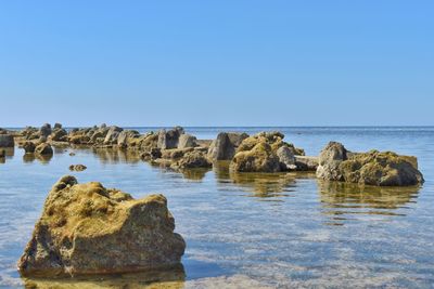 Rock formations in sea against clear blue sky