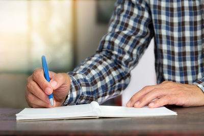 Midsection of man writing in book on desk