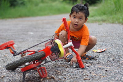 Portrait of cute boy with bicycle crouching on road