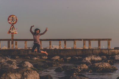 People on rock by sea against clear sky