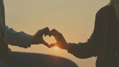 Couple forming heart shape against sky during sunset