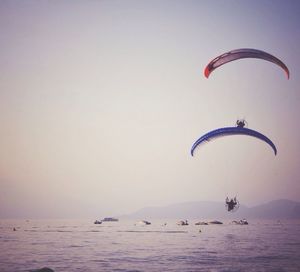 Low angle view of paragliders over sea against clear sky