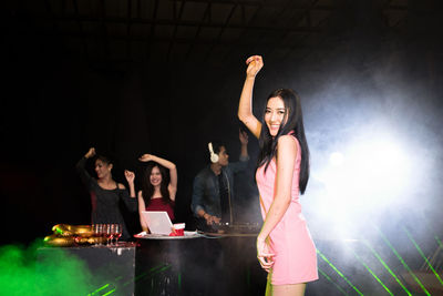 Portrait of happy young woman dancing against friends and dj in nightclub