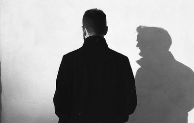 Rear view of silhouette man standing against white wall