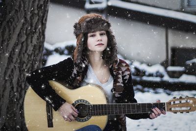 Portrait of woman playing guitar during snowfall