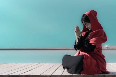 Young woman meditating on pier over sea against clear blue sky