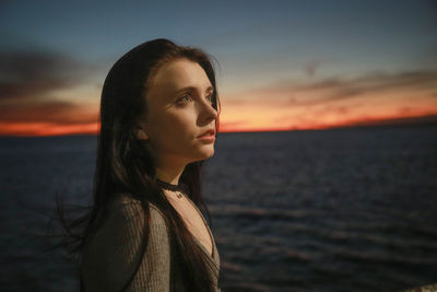 Close-up of young woman standing by sea against sky during sunset