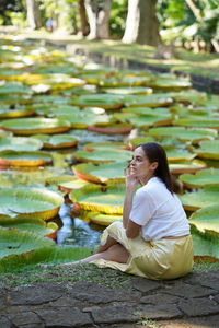 Thoughtful woman sitting by pond covered with lily pads