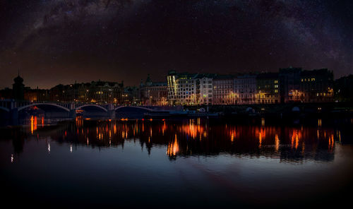 Illuminated buildings by river against sky at night