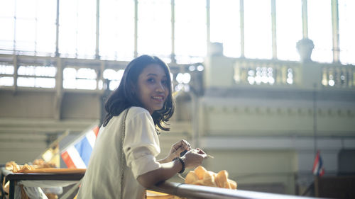 Portrait of smiling young woman standing against built structure