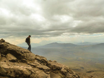 Rear view of man standing on mountain against cloudy sky