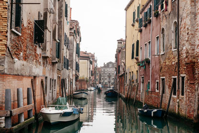 Boats moored on canal amidst buildings against sky