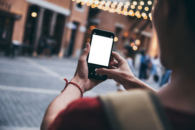 Midsection of person photographing with mobile phone in city