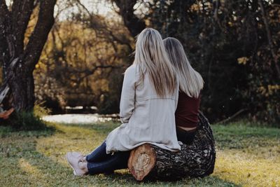 Rear view of women sitting on log