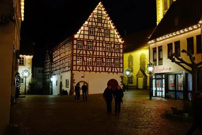 People walking on illuminated street amidst buildings at night