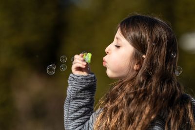 Side view of girl blowing bubbles in park