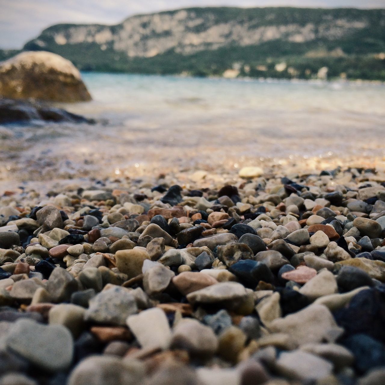 pebble, beach, stone - object, surface level, water, shore, rock - object, selective focus, stone, tranquility, nature, large group of objects, abundance, sea, tranquil scene, focus on foreground, beauty in nature, scenics, day, outdoors