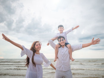 Portrait of cheerful family standing at beach against sky