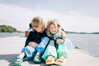 Happy friends sitting on shore against sea