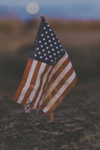 Close-up of weathered miniature american flag on field during sunset