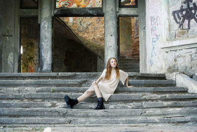 Full length of cute girl sitting on steps against abandoned building