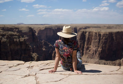 Full length of woman wearing hat while sitting on cliff against rock formations