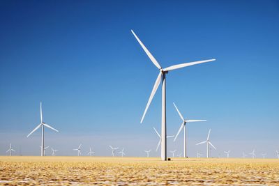 Windmills on landscape against blue sky