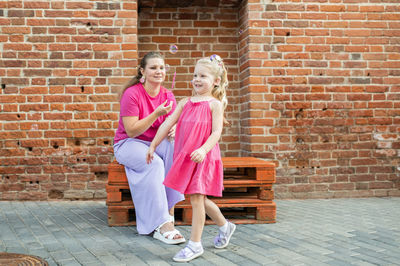 Portrait of young woman standing against brick wall