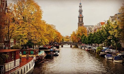 People by river in city against sky during autumn