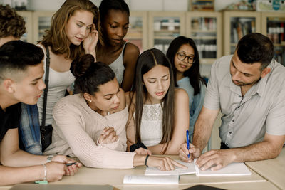 Professor teaching male and female students while leaning over table in classroom