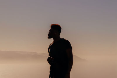 Man looking away while standing against sky during sunset