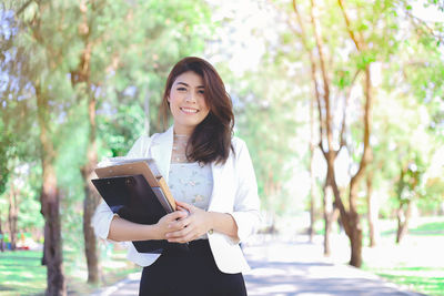 Portrait of smiling young woman standing against trees