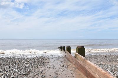 Wooden posts on beach against sky