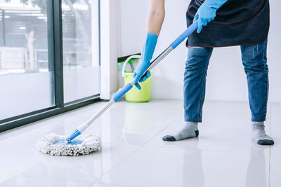 Low section of person cleaning tiled floor with mop
