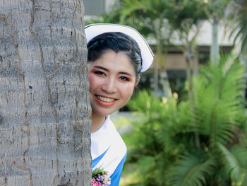 Portrait of smiling young woman against tree trunk