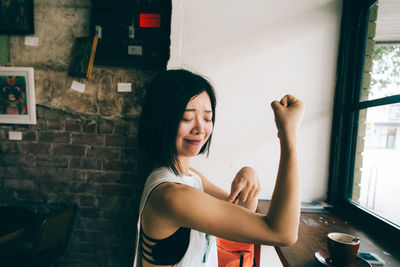 Smiling woman gesturing on muscles while sitting at cafe