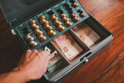 Cropped hand on mid adult man taking money from box on table