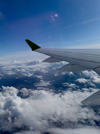 Aerial view of airplane flying over clouds against blue sky