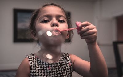 Close-up of cute girl blowing bubbles at home