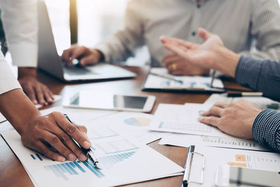 Midsection of colleagues analyzing graphs on table