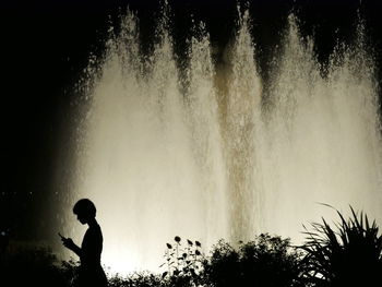 Silhouette man standing by waterfall against trees