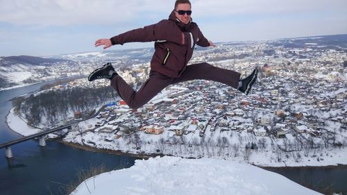 Full length of man jumping on snow against cityscape and sky