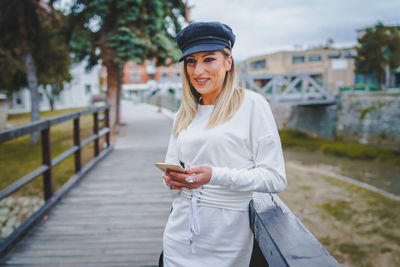 Young woman using mobile phone while standing on bridge