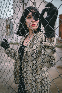 Portrait of young woman standing by chainlink fence